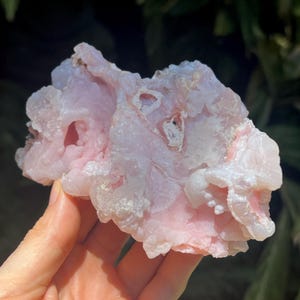 May include: A raw, pale pink mineral specimen with a botryoidal, bubbly texture and translucent crystalline formations. The stone features irregular, organic shapes with varying shades of soft rose and white, showcasing a natural, unpolished surface.