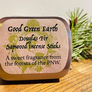 May include: A silver tin with a label that reads "Good Green Earth Douglas Fir Sapwood Incense Sticks" and "A sweet fragrance from the forests of the PNW."