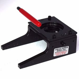 May include: Black circle punch with a red handle. The punch is labeled "CIRCLE PUNCH MODEL 2625 Manufactured in the USA by TECHNE POND DU LAC, WI"