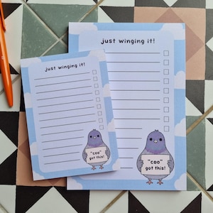 May include: Two rectangular paper notepads with a light blue sky and white cloud background. Each notepad features the text "just winging it!" at the top, horizontal lines, a checklist, and a cartoon pigeon holding a sign that says "coo got this!"