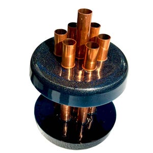 Könnte beinhalten: Eine schwarze und blaue Keramikvase mit einem Design aus Kupferrohren. Die Vase hat einen runden Boden und einen zylindrischen oberen Teil mit mehreren herausragenden Kupferrohren.