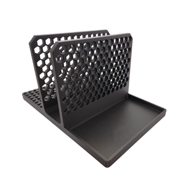 May include: A black desk organiser with a honeycomb pattern on the sides and a tray at the base. The organiser has two vertical sections and a flat base, suitable for holding papers, mail, or office supplies.