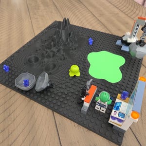 May include: A Lego space scene on a black baseplate. The scene includes a gray mountain, a green blob, a crane, and several Lego figures and accessories. The color palette is primarily gray, black, green, and blue.