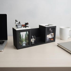 May include: Black desk organizer with two picture frames, a pen holder, and a small shelf. The organizer is decorated with Lego figures and a Lego base. One frame displays a forest scene, the other a coffee cup.