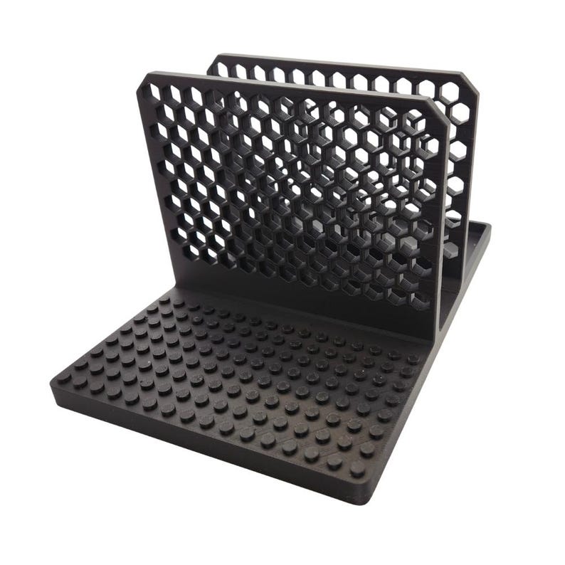 May include: A black desk organiser with a honeycomb pattern on the upright sections and a studded base. The organiser is made of a matte black material and is designed to hold items upright.