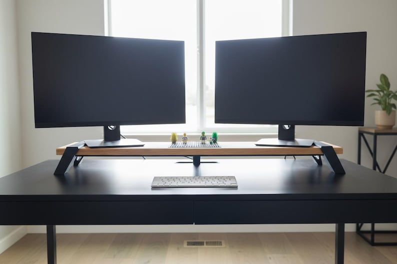 Pode incluir: Uma secret&aacute;ria preta com dois grandes monitores de computador, um teclado e um suporte de monitor de madeira. O suporte tem pernas pretas e cont&eacute;m pequenas figuras de Lego. A secret&aacute;ria est&aacute; em frente a uma janela.