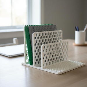 May include: A white desk organizer made of interlocking blocks, featuring a honeycomb design. It holds green and gray blocks. Pens and pencils are in a white cup in the background. A laptop is visible on the desk.