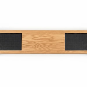 Pode incluir: Um objeto retangular de madeira clara, com duas almofadas pretas texturizadas e suportes de metal preto. O objeto tem aproximadamente 76 cm de comprimento.