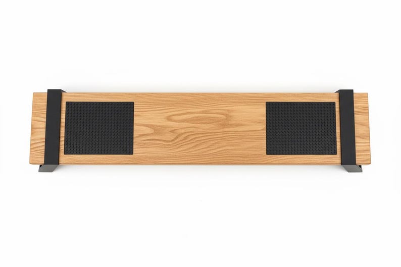 Pode incluir: Um objeto retangular de madeira clara, com duas almofadas pretas texturizadas e suportes de metal preto. O objeto tem aproximadamente 76 cm de comprimento.