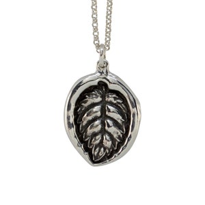 May include: A silver necklace with a pendant featuring a detailed leaf design. The pendant is round and has a textured surface.