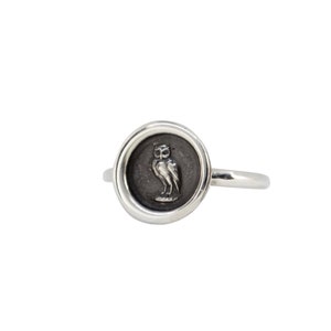 May include: A silver ring with a round, black enamel bezel featuring an engraved image of an owl.