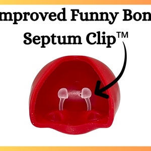 Op de afbeelding: Een rode septumclip met de tekst "Improved Funny Bone Septum Clip&trade;". De clip heeft twee doorzichtige, gebogen pinnen. Het product is ontworpen om in de neus te worden geplaatst.