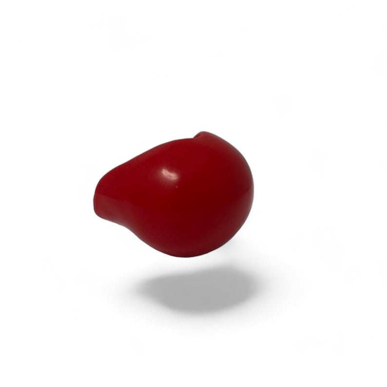 Op de afbeelding: Een glanzend, rood, druppelvormig object, mogelijk een decoratief element of onderdeel van een groter item. Het object zweeft in de lucht en werpt een schaduw op een witte achtergrond.