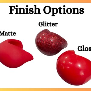 Op de afbeelding: Afbeelding met drie rode objecten met verschillende afwerkingen: mat, glitter en glans. De tekst "Finish Options" staat bovenaan. Het matte object is effen rood, het glitterobject is glinsterend rood en het glansobject heeft een glanzende rode afwerking.