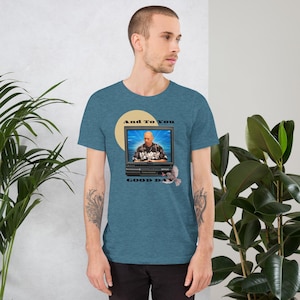 Puede incluir: Camiseta de manga corta de color turquesa con un gráfico de una persona en una pantalla de ordenador y el texto "And To You GOOD DAY". El gráfico incluye un círculo amarillo y un diseño floral. La camiseta es de material suave.