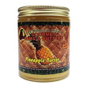 May include: A glass jar with a gold lid filled with pineapple butter. The label reads "Les Menehune Kitchen Gourmet Jams & Butters Pineapple Butter Made in Hawaii".