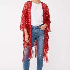 Op de afbeelding: Een felrode kimono met open voorzijde, gemaakt van doorschijnende mesh-stof versierd met verspreide witte pailletten. Het kledingstuk heeft wijde driekwartmouwen en een lange, rechte zoom afgewerkt met decoratieve franjes.