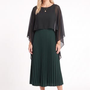 May include: A midi-length dress featuring a dark green pleated skirt and a black sheer chiffon cape-style overlay bodice with a round neckline. The garment is paired with black pointed-toe high-heeled pumps and gold-toned jewelry accessories.