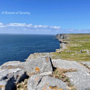 May include: A scenic view of a rocky cliff overlooking a vast blue ocean. The sky is clear and blue with a few white clouds. The text "A Moment of Serenity" is written in white at the top of the image.