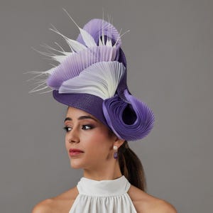 May include: A striking purple and white pleated hat with feather detailing. The hat has a wide brim and a sculptural design. This statement hat is suitable for special occasions and events.