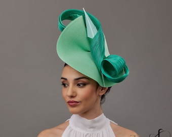 May include: A green and light green fascinator with a large, curled brim and a smaller, curled accent piece. The fascinator is made of a straw-like material.