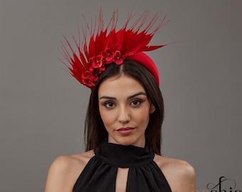 May include: A red felt headband with a large red feather and flower embellishment. The headband is worn by a person with dark hair.