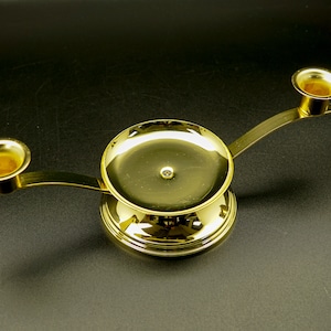 May include: A gold metal candle holder with two arms and a round base. The holder has a smooth, polished finish.