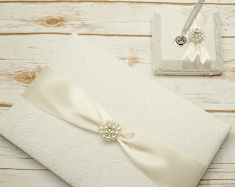 May include: White lace guest book with a satin ribbon and pearl embellishment. A matching pen holder with a pearl embellishment and a pen is also included.