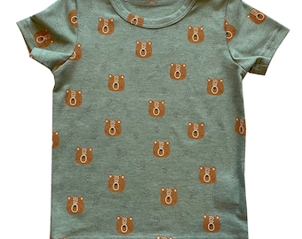 Puede incluir: Una camiseta verde de manga corta con un estampado de osos marrones por todas partes. Los osos miran hacia adelante y tienen un diseño sencillo.