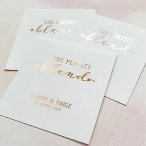 May include: Three white cards with gold foil lettering. The top card says "The Perfect Blend". The middle card says "The Perfect Blend". The bottom card says "The Perfect Blend" and "Aaron & Paige 27 August 2023".