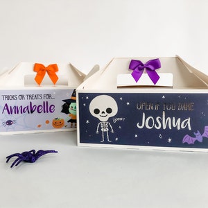 May include: Two Halloween treat boxes with personalized names. The box on the left has a witch and pumpkin design and says "Tricks or treats for... Annabelle". The box on the right has a skeleton and bat design and says "Open if you dare Joshua".
