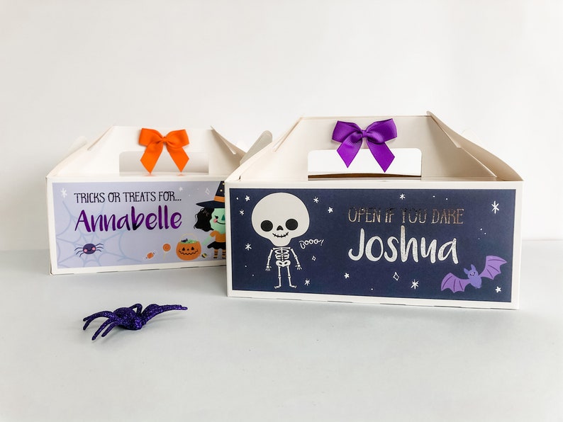 May include: Two Halloween treat boxes with personalized names. The box on the left has a witch and pumpkin design and says "Tricks or treats for... Annabelle". The box on the right has a skeleton and bat design and says "Open if you dare Joshua".