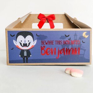 May include: A brown cardboard box with a vampire illustration and the text "Beware this box bites Benjamin". The box has a red ribbon on top and is decorated with bats and a moon.