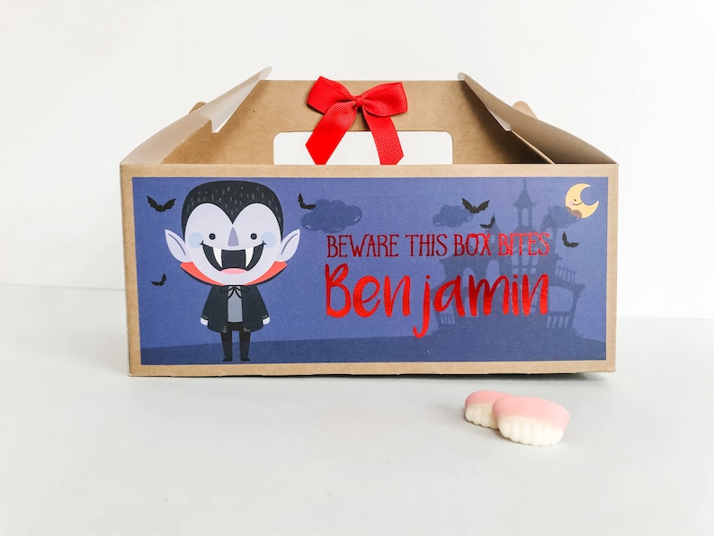 May include: A brown cardboard box with a vampire illustration and the text "Beware this box bites Benjamin". The box has a red ribbon on top and is decorated with bats and a moon.