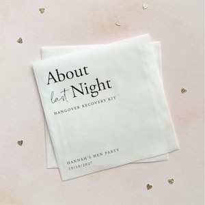 May include: A white square paper envelope featuring black printed text that reads About last Night HANGOVER RECOVERY KIT, followed by HANNAH'S HEN PARTY and the date 19/10/2027. The envelope is surrounded by small gold heart-shaped confetti.