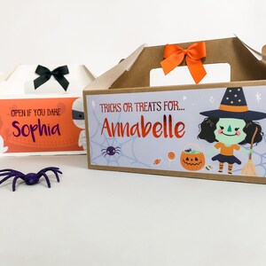 May include: Two Halloween treat boxes with personalized names. The first box is orange and white with the text "Open if you dare Sophia". The second box is brown with a witch illustration and the text "Tricks or treats for... Annabelle".