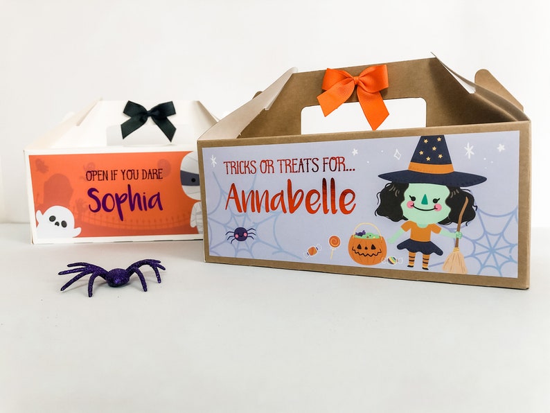 May include: Two Halloween treat boxes with personalized names. The first box is orange and white with the text "Open if you dare Sophia". The second box is brown with a witch illustration and the text "Tricks or treats for... Annabelle".