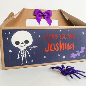 May include: A brown cardboard Halloween treat box with a purple bow. The box has a blue background with a white skeleton, a purple bat, and the text "Open if you dare Joshua".