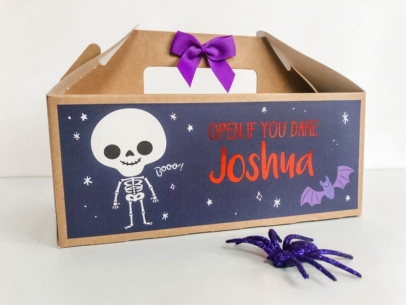 May include: A brown cardboard Halloween treat box with a purple bow. The box has a blue background with a white skeleton, a purple bat, and the text "Open if you dare Joshua".