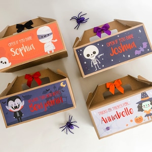 May include: Four brown cardboard Halloween treat boxes with colorful designs and names. The boxes have cut-out handles and are decorated with images of a mummy, a skeleton, a vampire, and a witch. The boxes have the names "Sophia", "Joshua", "Benjamin", and "Annabelle" printed on them.
