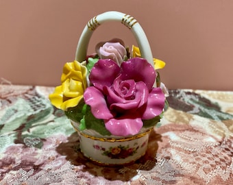 Könnte beinhalten: Ein Keramikkorb gefüllt mit bunten Rosen. Der Korb hat einen weißen Griff mit goldenen Akzenten und ist mit gelben, rosa und roten Rosen geschmückt. Der Boden des Korbes ist weiß mit einem floralen Muster und goldenem Rand.