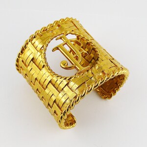 May include: A gold-tone woven cuff bracelet with a large, raised, interlocking "TJ" monogram.