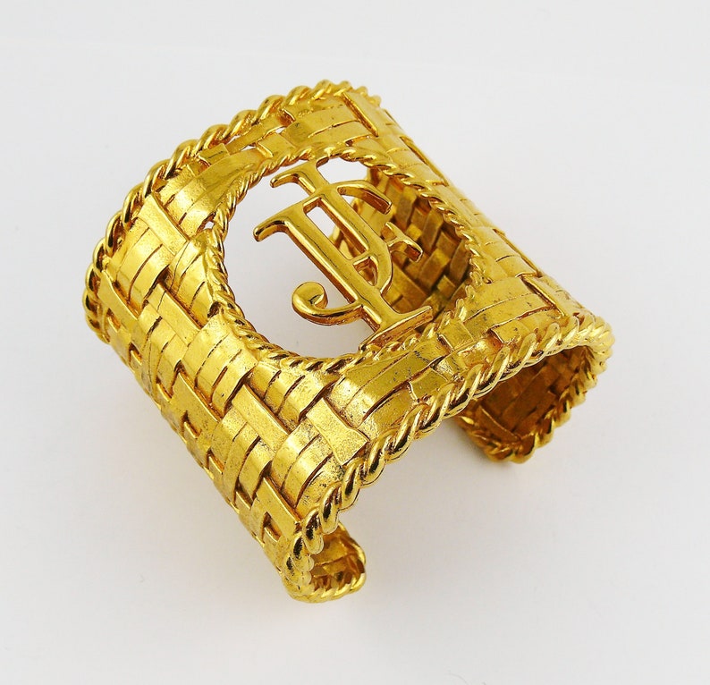 May include: A gold-tone woven cuff bracelet with a large, raised, interlocking "TJ" monogram.