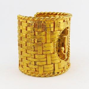 May include: A gold-toned woven cuff bracelet with a large, raised, gold-toned 'J' logo on the side.