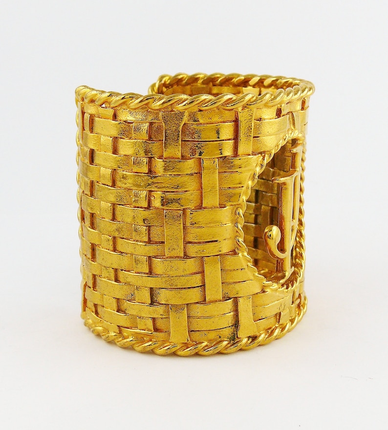 May include: A gold-toned woven cuff bracelet with a large, raised, gold-toned 'J' logo on the side.
