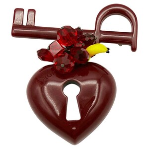 May include: A red heart-shaped lock with a keyhole and a key attached. The key is decorated with red and yellow crystals. The lock has the word "Dior" inscribed on it.