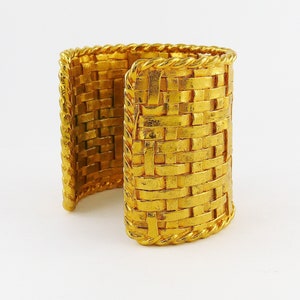 May include: A gold-tone woven cuff bracelet with a rope-like edge.