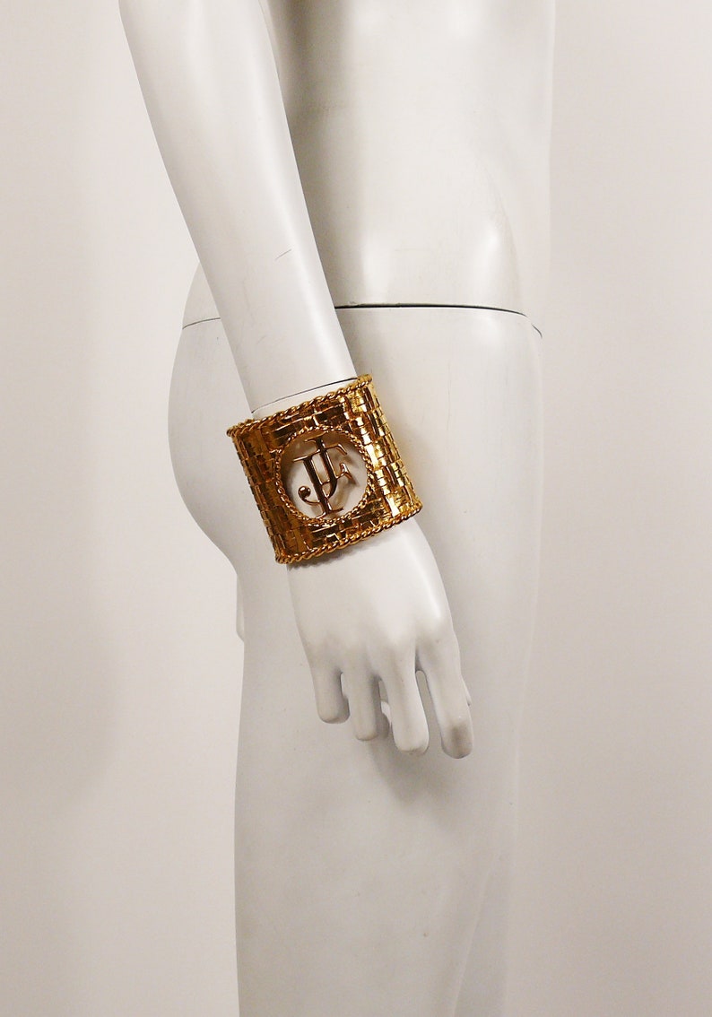 May include: Gold-toned metal bracelet with a woven design and a large, open, circular cutout featuring the letters "JF".