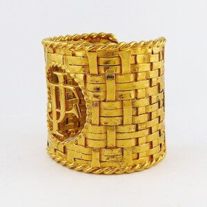 May include: A gold-tone woven cuff bracelet with a large, cutout "F" monogram. The bracelet is made of a thick, textured metal and has a wide, open design.