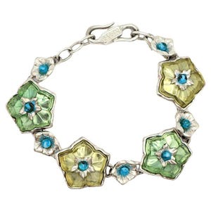 May include: A silver bracelet with a chain link design and flower-shaped charms. The charms are made of green, yellow, and clear glass with blue accents. The bracelet has a clasp that says "KENZO" on it.